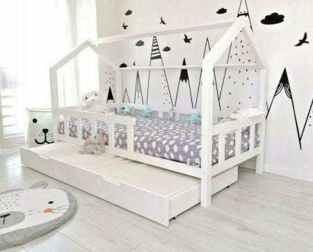 Children's house-shaped bed with a white frame and gray mattress in a room with black wall decals.