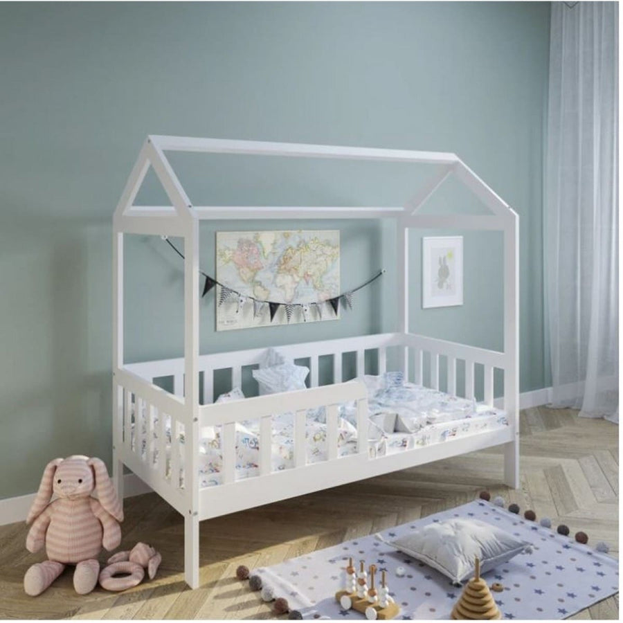 White children's house bed in a room with toys and decor.